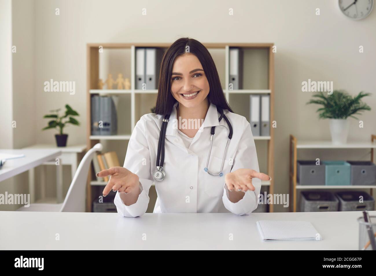 Lächelnde Frau Arzt Blick auf die Kamera und zeigt etwas mit Hände in der medizinischen Klinik Stockfoto