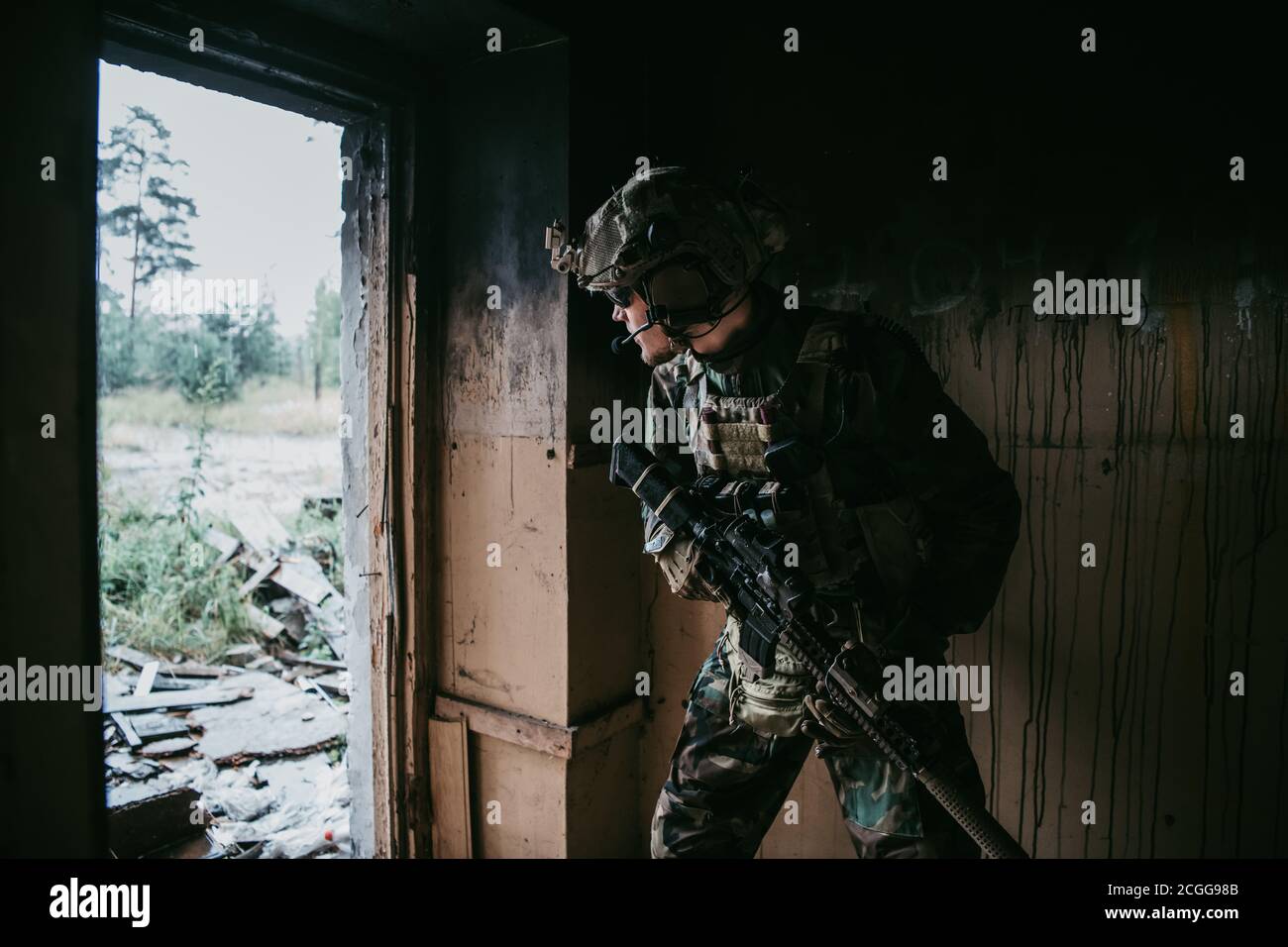Soldat in voller US MARSOC bewaffnet mit Sturmgewehr durch das verlassene Gebäude laufen. Militärischer Zusammenstoß. Stockfoto