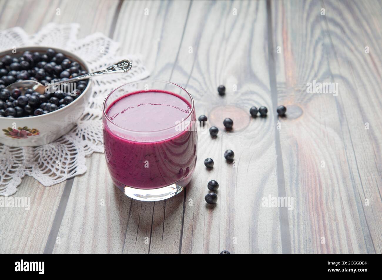 Auf einem hölzernen Hintergrund ist ein Glas mit einer Diät Trinken Heidelbeer Smoothie und einen Teller mit Heidelbeeren auf einem Spitze Serviette .Ort für Kopie Raum Stockfoto