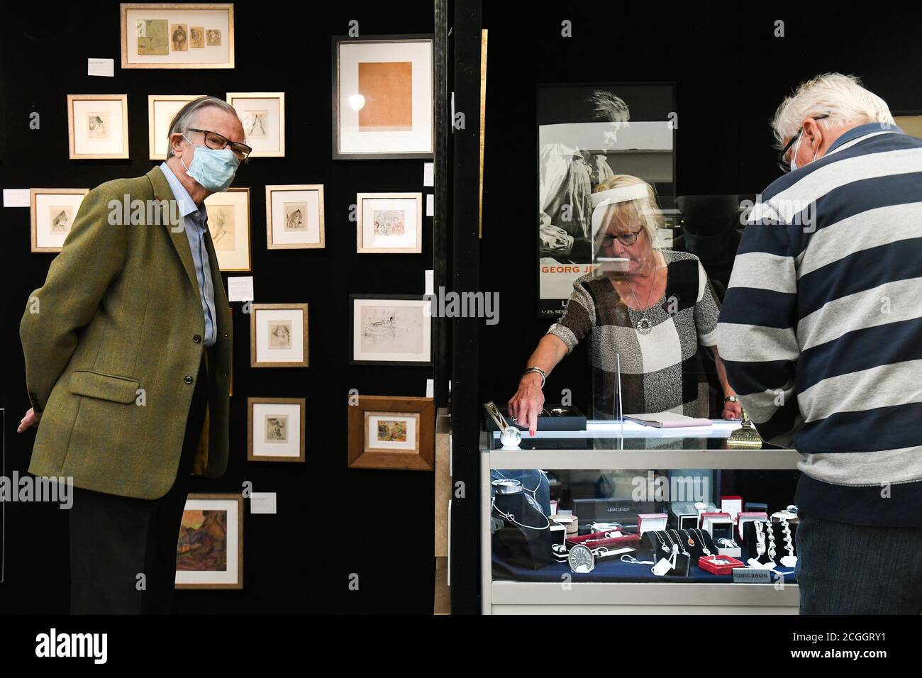 Ein Kunsthändler bedient Kunden von hinter einem Kunststoffschirm auf der Petworth Park Antiquitäten und Kunstmesse, im Petworth House in West Sussex. Stockfoto