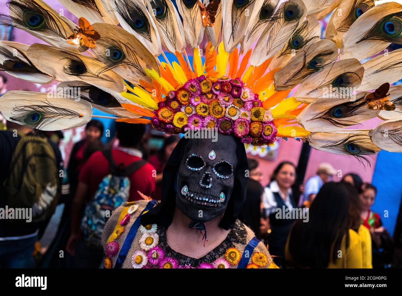 Eine Mexikanerin, die eine Totenkopfmaske mit Federkopfschmuck trägt, tritt auf der Straße während der Feierlichkeiten zum Tag der Toten in Oaxaca, Mexiko, auf. Stockfoto