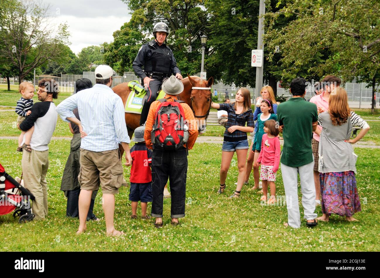 Ein männlicher Polizist, der auf dem Pferderücken reitet und mit Bewohnern des Trinity-Bellwoods Park in der Innenstadt von Toronto, Ontario, Kanada, spricht. Stockfoto