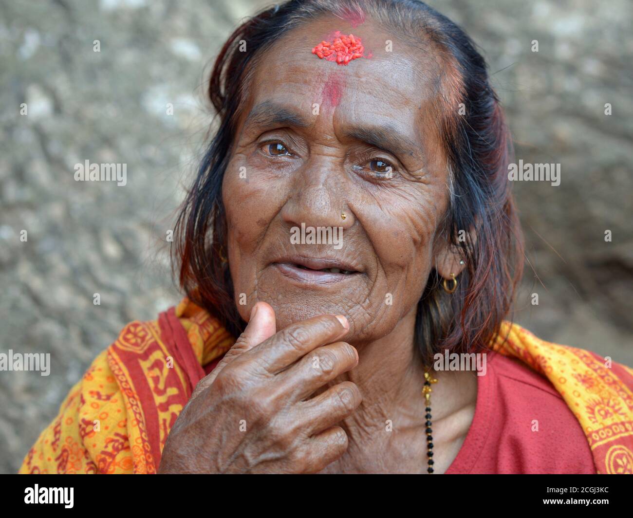 Die alte nepalesische Bettlerin und Hindu-Anhängerin mit roter Reistilak-Markierung auf ihrer Stirn berührt ihr Kinn. Stockfoto