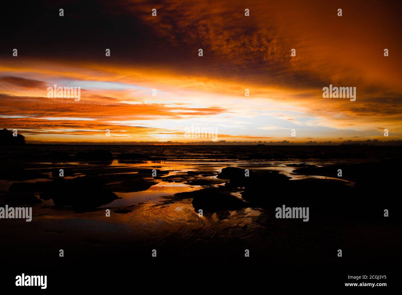 Blick vom tropischen Strand über Steine auf dramatische orange gelbe Sonnenuntergang über andamanensee mit Sturmwolken, ko lanta, Thailand (Fokus auf Horizont) Stockfoto
