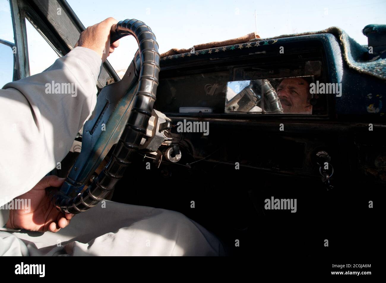 Ein ägyptischer Taxifahrer hält das Lenkrad, sein Gesicht spiegelt sich auf einem Armaturenbrett-Spiegel, in seinem Taxi in Kairo, Ägypten. Stockfoto