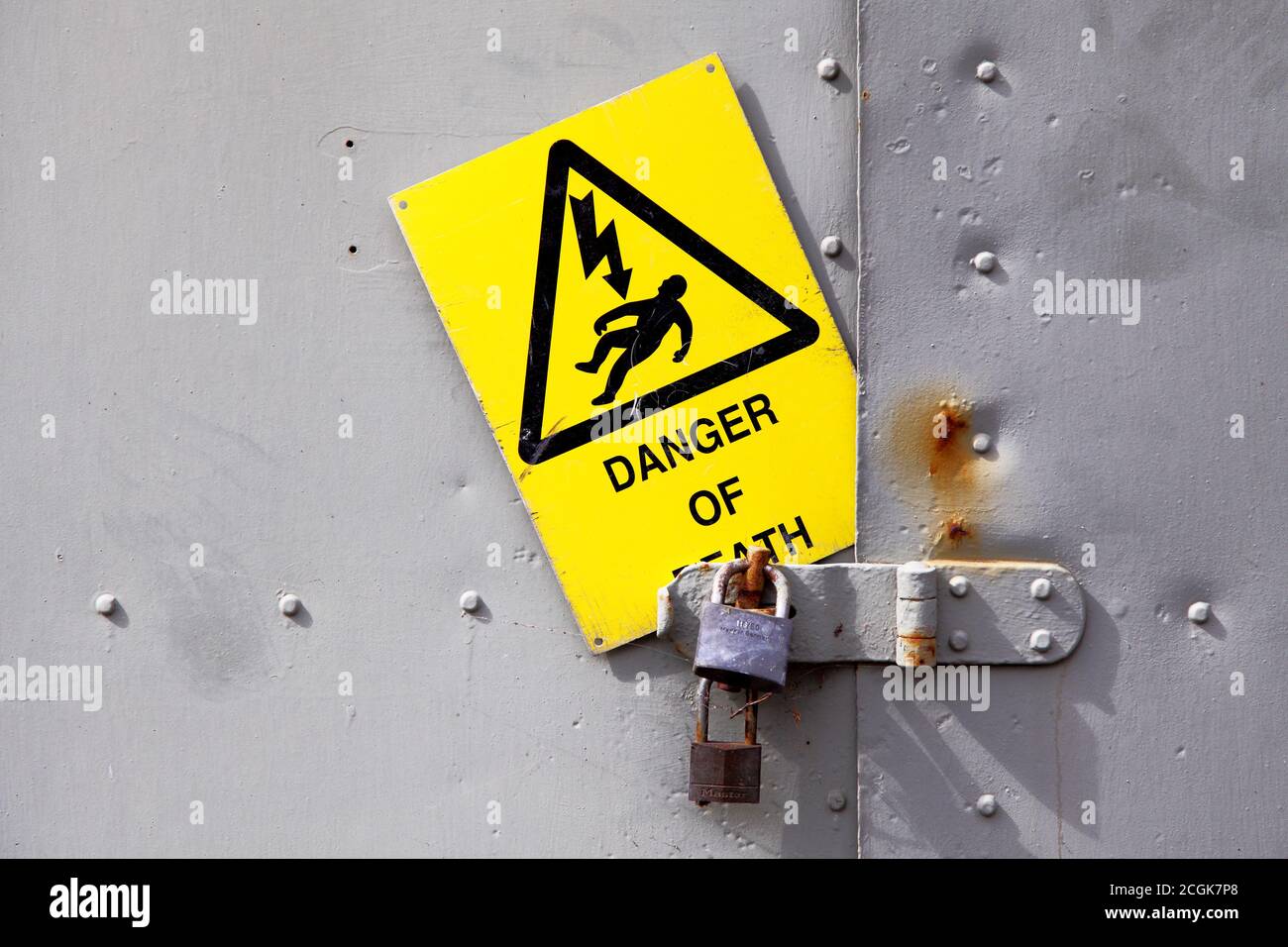Mit Vorhängeschloss verriegelte Tür aus verstärktem Stahl aus Metall mit gelbem Warnschild für Todesgefahr einschließlich Stromschlag-Symbol. Stockfoto