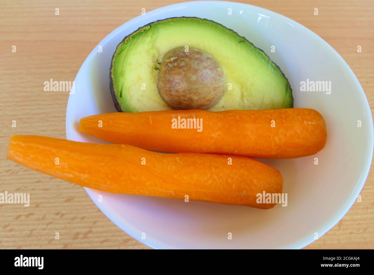 Gesunde Saft Zutaten - Nahaufnahme Hälfte Avocado und Karotten in Eine weiße Schale auf einem Tisch Stockfoto