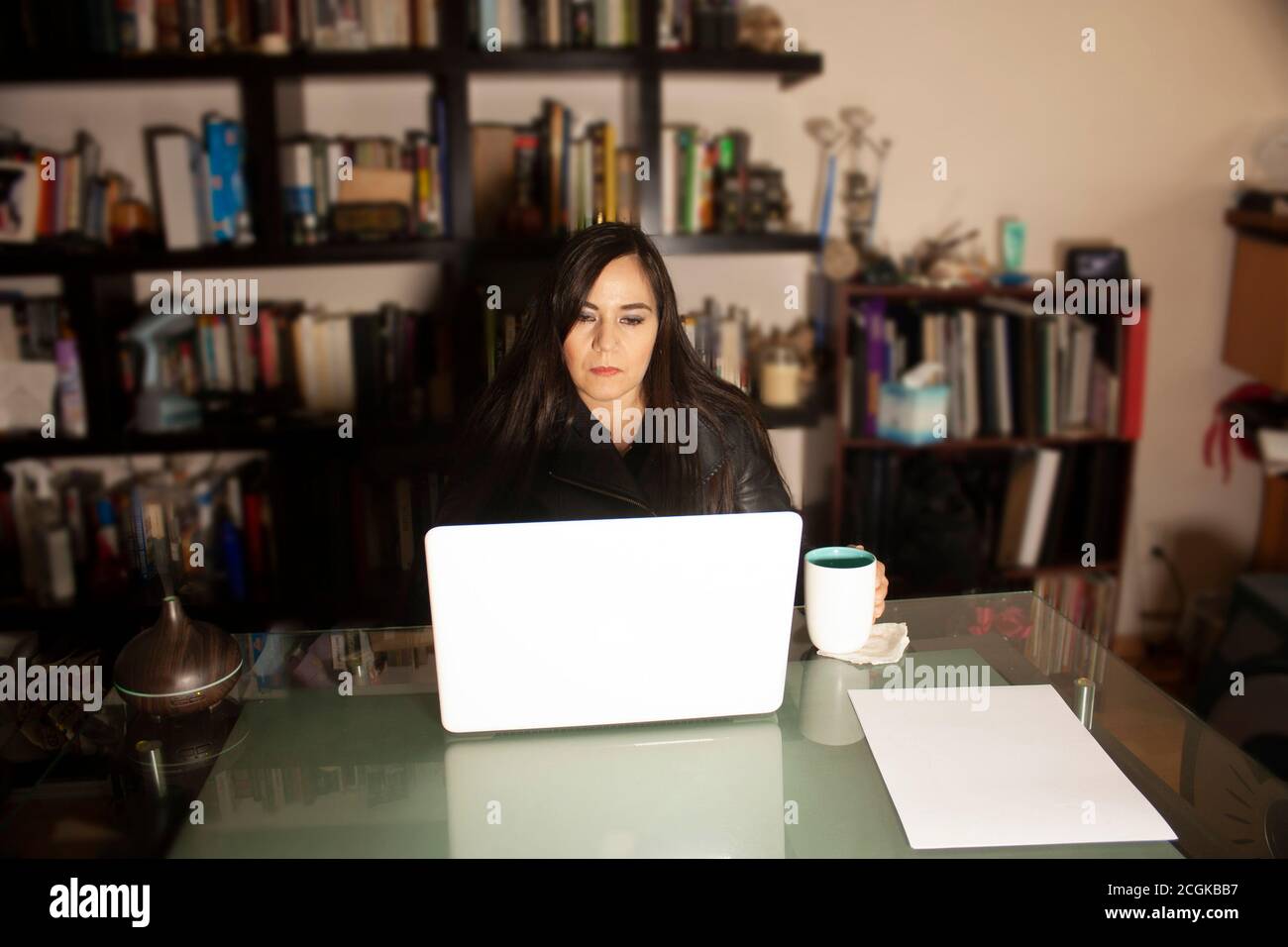 Frau, die zu Hause mit einem Laptop arbeitet, während sie von begleitet wird Eine Tasse Kaffee umgeben von Büchern entspannt die Umgebung Mit einem arom Luftbefeuchter Stockfoto