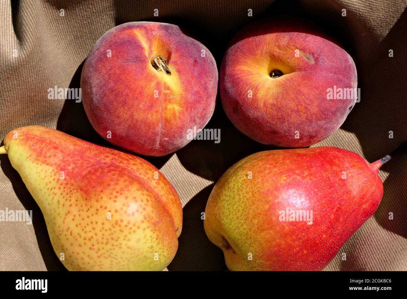 Nahaufnahme zwei sonnenbeschienenen rötlichen Birnen und Pfirsiche auf einem braunen Stoff Stockfoto