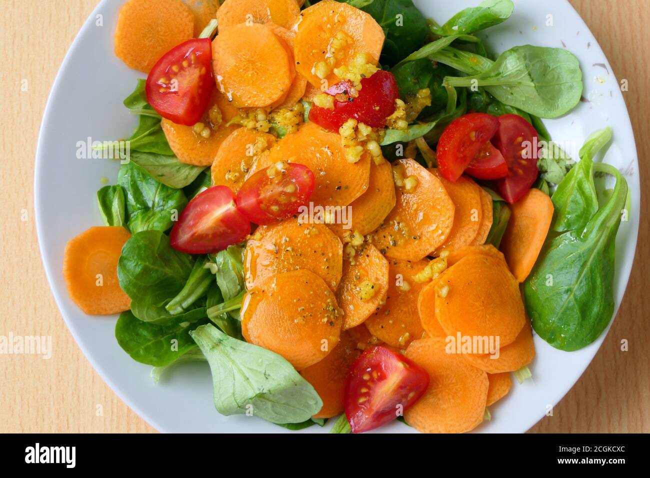 Luftaufnahme eines gesunden vegetarischen hausgemachten Salats mit Nusssalat oder Lammsalat, Karottenscheiben, Tomaten und Knoblauch auf einem weißen Teller Stockfoto