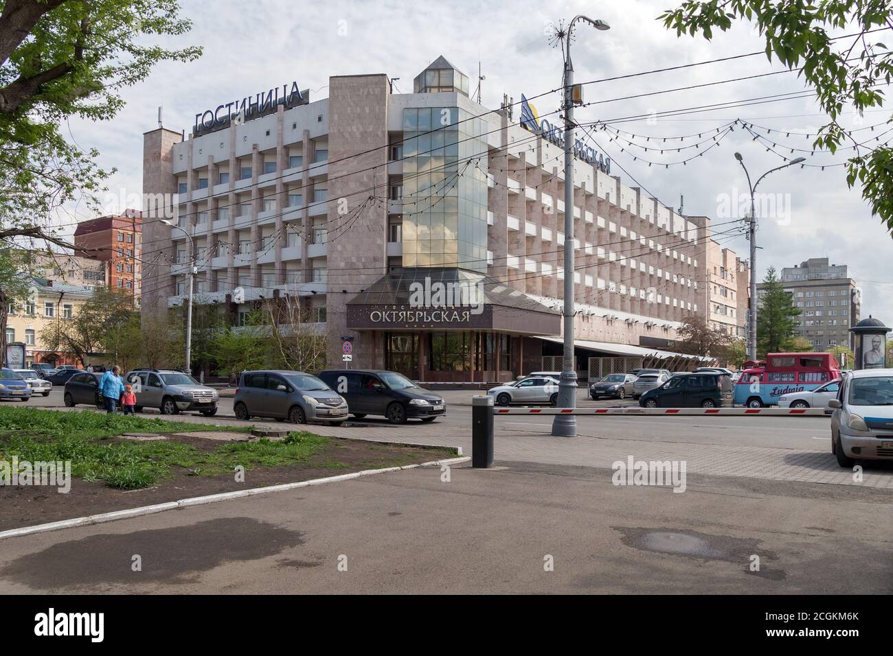 Oktyabrskaya Hotel mit Autos davor auf Mira Avenue in der Altstadt von Krasnojarsk an einem bewölkten Frühlingstag. Stockfoto