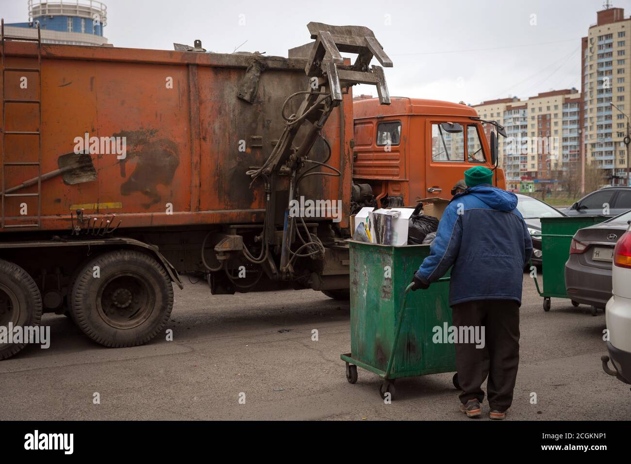 Während der Müllabfuhr auf den Straßen von Krasnojarsk trägt der Arbeiter einen Container mit Müll zur Müllabfuhr. Stockfoto