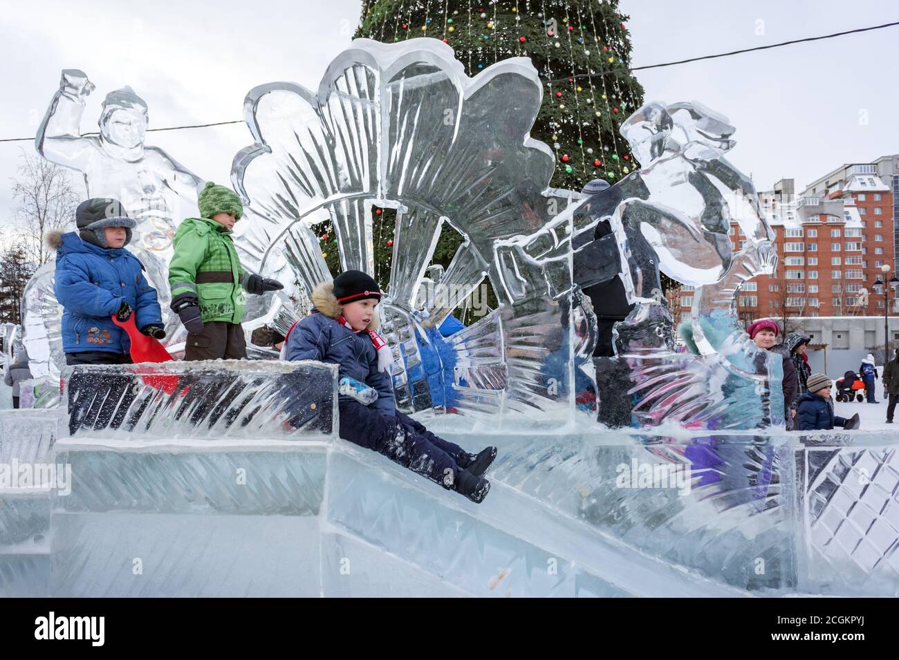 Kinder reiten mit einer Eisrutsche auf dem Hintergrund Weihnachtsbaum im Zentrum Krasnojarsk Stadt während der Winter Neujahr. Krasnojarsk Terri Stockfoto