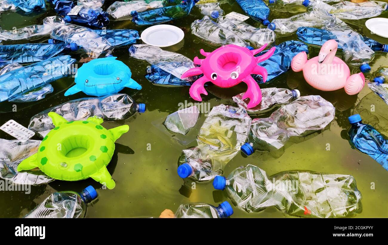 Verschmutzung der Umwelt. Plastikflaschen in Wasser und aufblasbares Spielzeug. Aufblasbare rosa Flamingos, grüne Schildkröte, blaue Fische, Himbeer-Krebse am Stockfoto