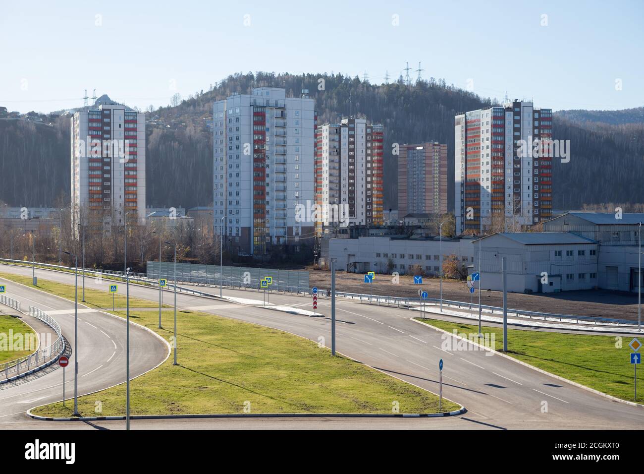 Städtisches Wohngebiet mit Häusern und Straßenkreuzung vor dem Hintergrund eines bewaldeten Berges, in Krasnojarsk im Herbst. Stockfoto