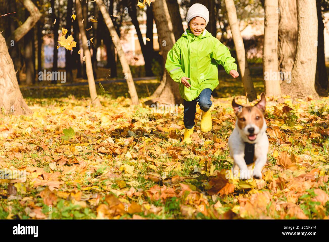Herbst Outdoor-Aktivitätskonzept mit kleinen glücklichen Jungen in grün Regenmantel läuft nach Haustier Hund im Herbst Park am September Tag Stockfoto