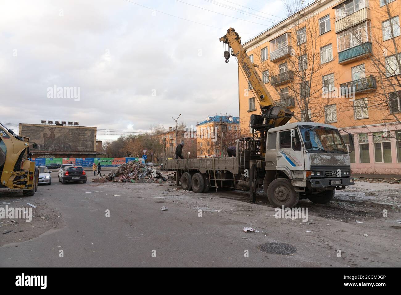 Arbeiter der öffentlichen Dienstleistungen stellen Bauabfälle aus dem Abriss Von alten Pavillons in einem LKW mit einem Kran in Eine Gasse in der Nähe eines Wohnhauses Stockfoto