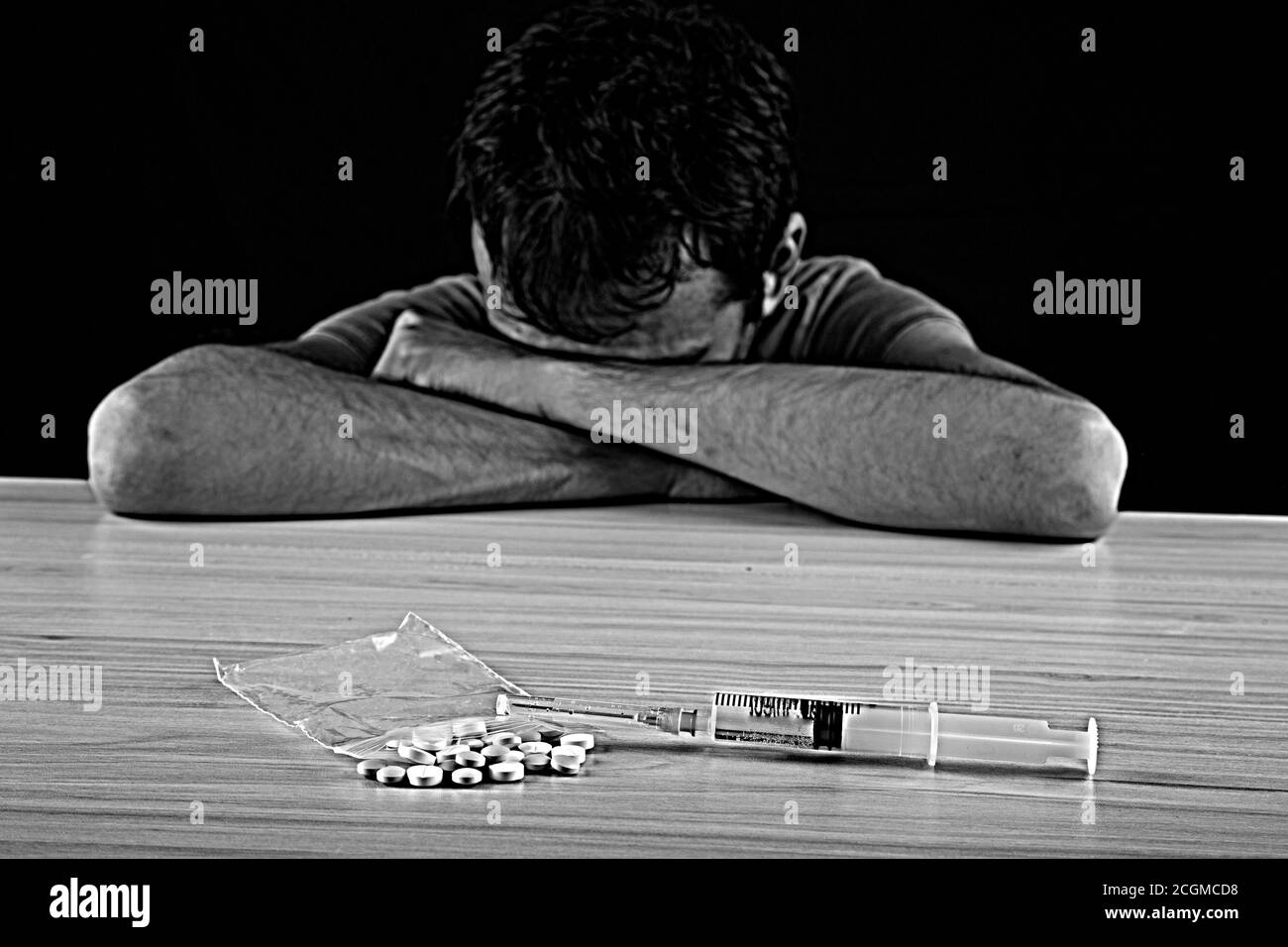 Männliche Drogenabhängige sitzen mit Spritze und Drogen aus Fokus im Hintergrund, Schwarzweiß-Foto Stockfoto