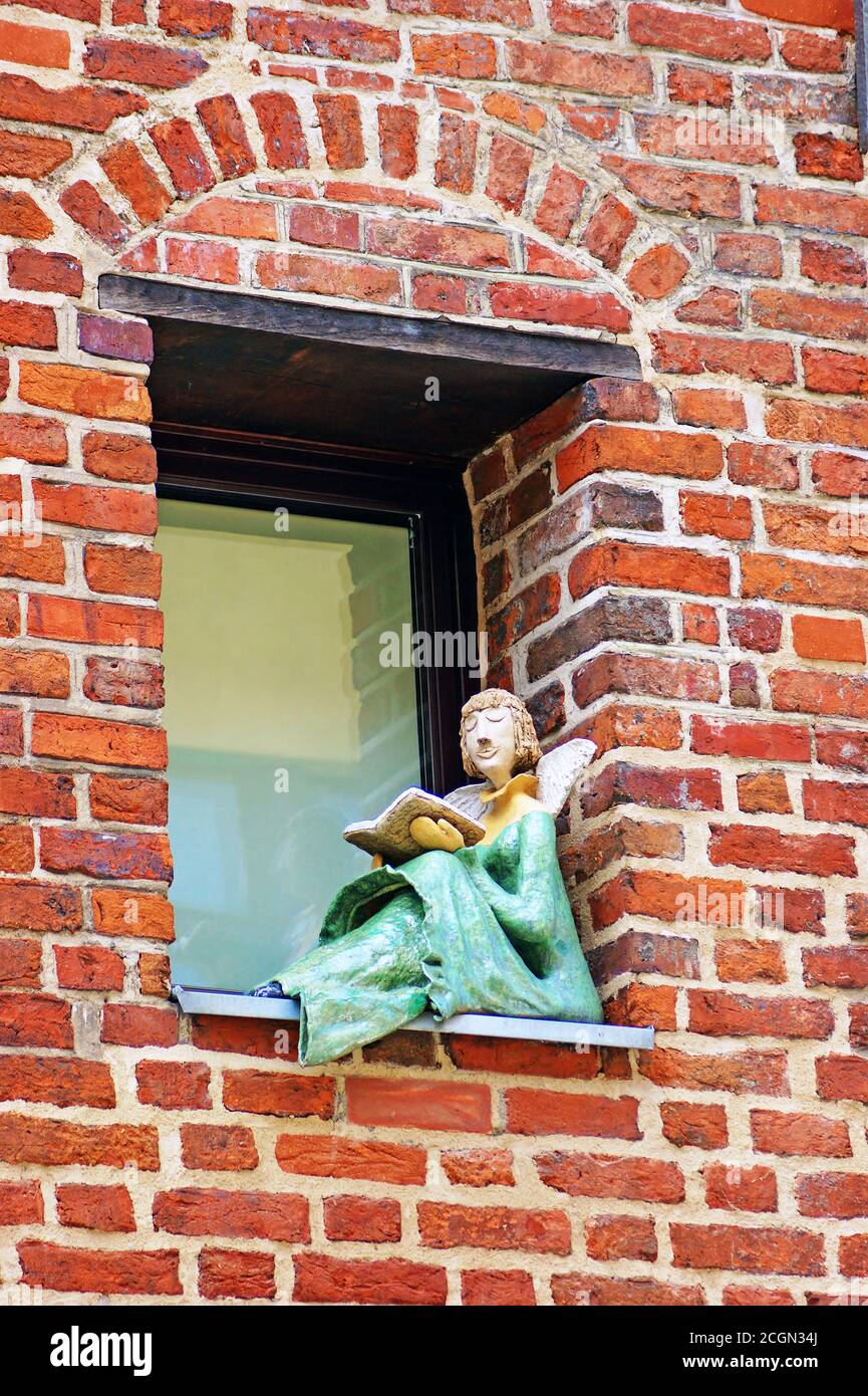 Ein Engel liest ein Buch, das auf der Fensterbank an der Außenseite eines Gebäudes in Torun, Polen, thront. Stockfoto