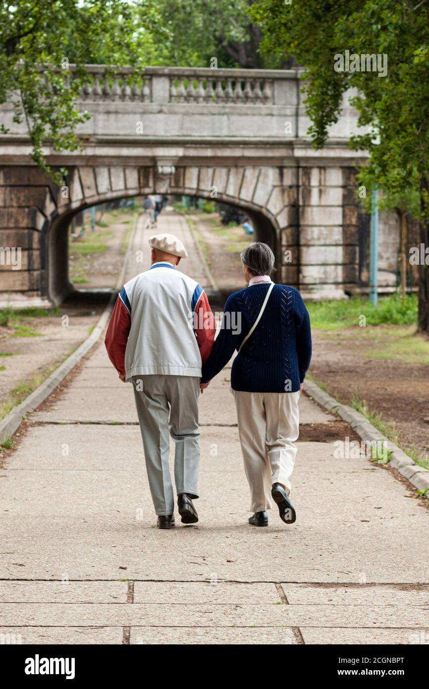 Gut gekleidete, lebhafte ältere Paare zeigen ihre Liebe, indem sie ihre Hände halten, während sie an einem schönen Nachmittag in einem Park im Zentrum von Paris spazieren. Stockfoto