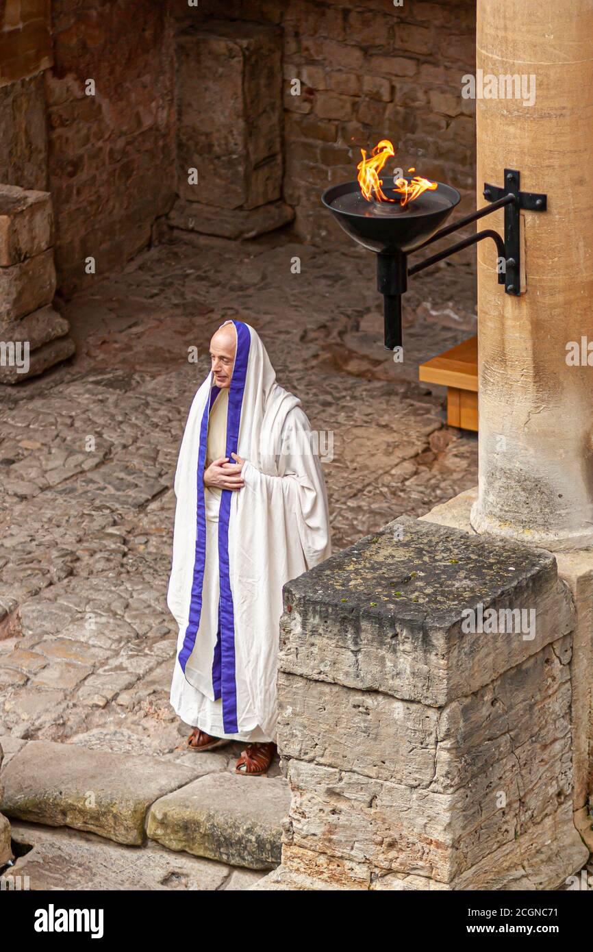 Bath, UK, 03/06/2010: Ein älterer kaukasischer Mann, der im antiken Rom wie ein Priester verkleidet ist, steht in einem historischen römischen Gebäude. Das Steingebäude h Stockfoto