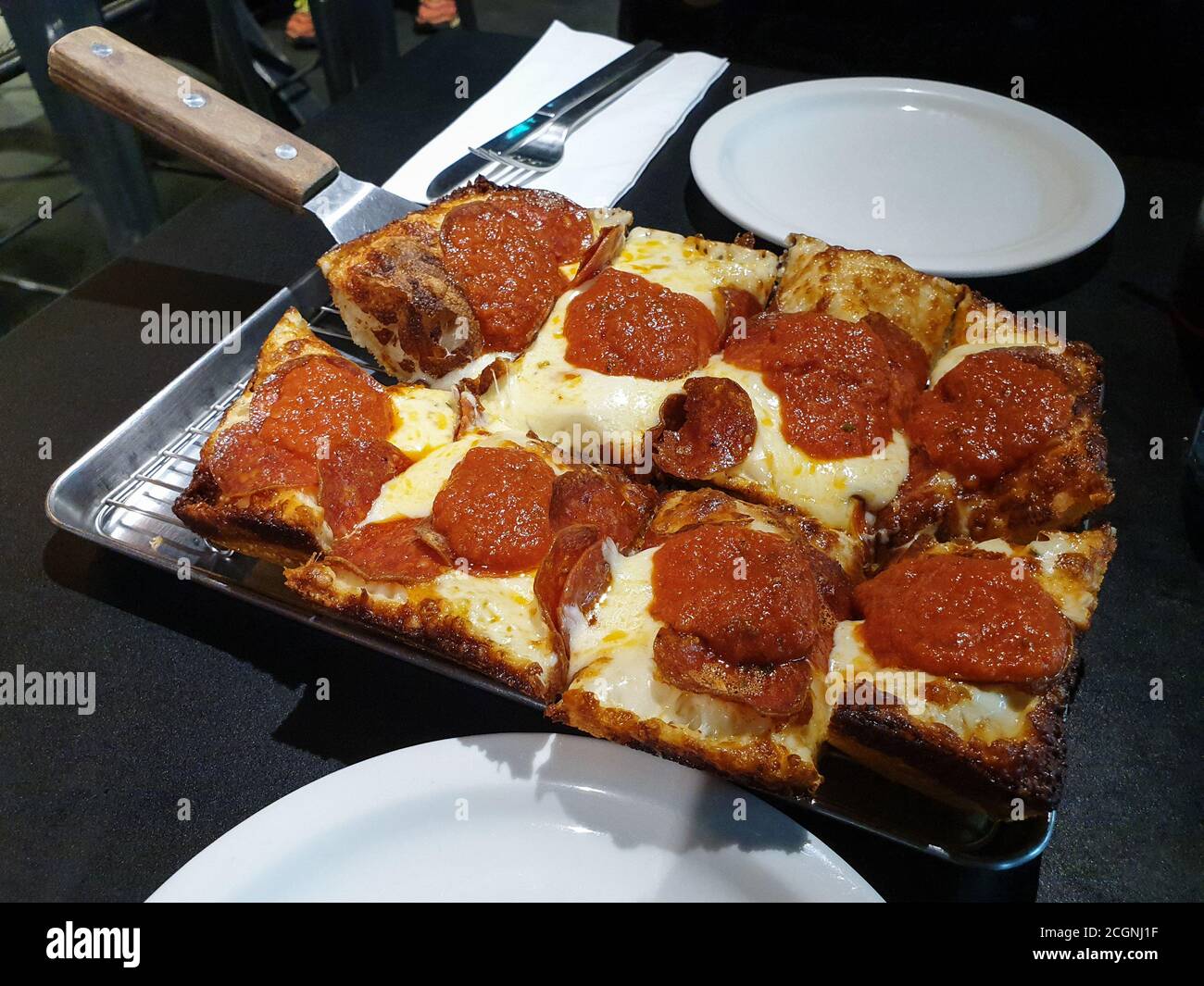 Pizza im Detroit-Stil. Rechteckige Pizza mit einer dicken knusprigen Kruste und Toppings wie Pepperoni. Gebacken in einer quadratischen Pfanne, die industrielle Teile Tablett ist Stockfoto