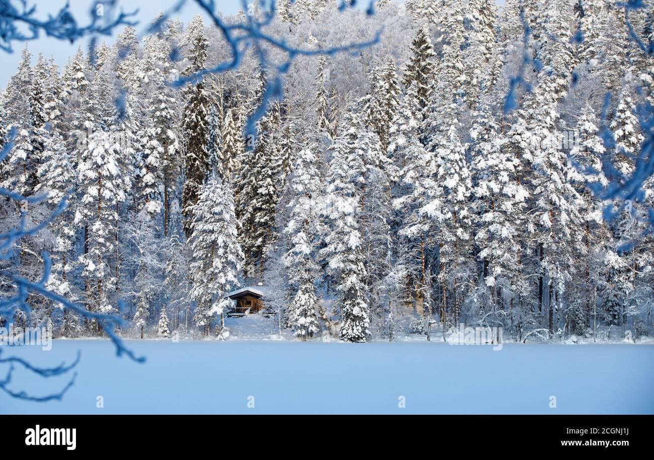 Kleine hölzerne Saunakabine aus Baumstämmen im verschneiten Wald an einem gefrorenen See im Winter, Finnland Stockfoto