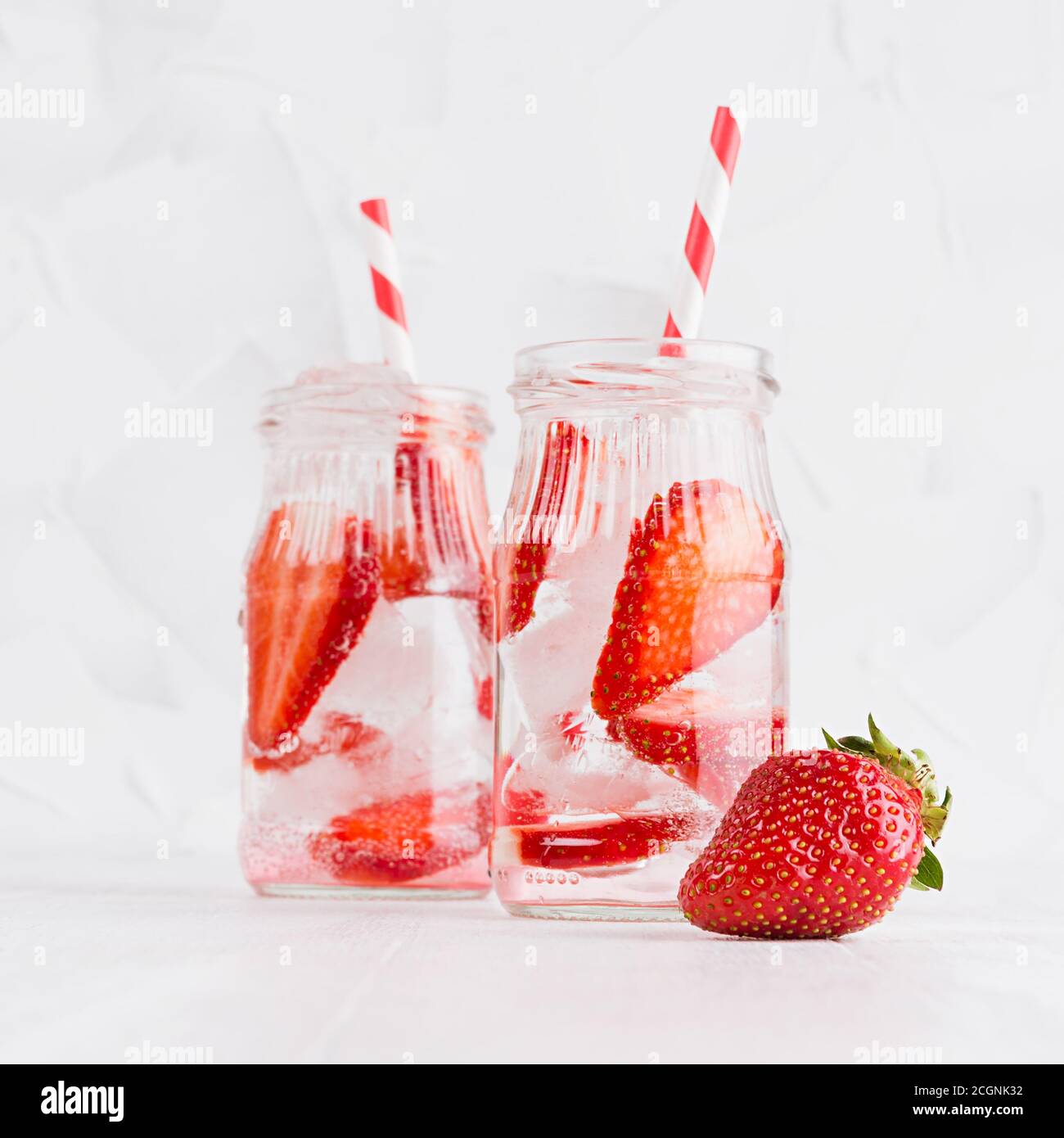 Kaltes frisches Fruchtgetränk von reifen Erdbeeren mit Eis, Sodawasser, Blasen, lustig gestreiftem Stroh auf einfachem weichen hellweißen Hintergrund, quadratisch. Stockfoto