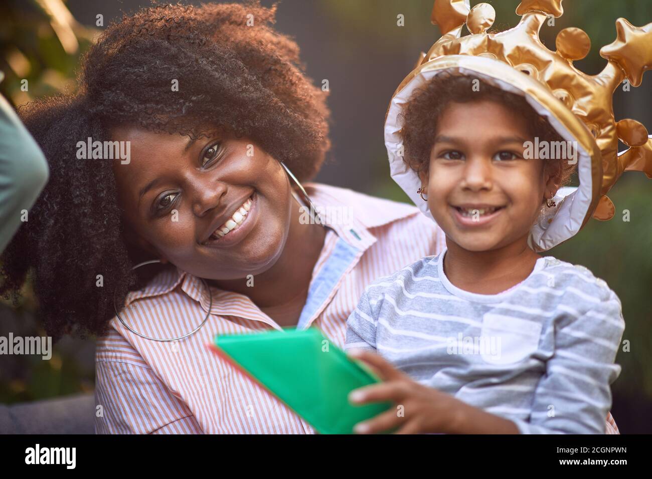 Kleines afro-amerikanisches Mädchen und ihre Mutter lächeln zusammen und beobachten die Kamera. Blickkontakt Stockfoto
