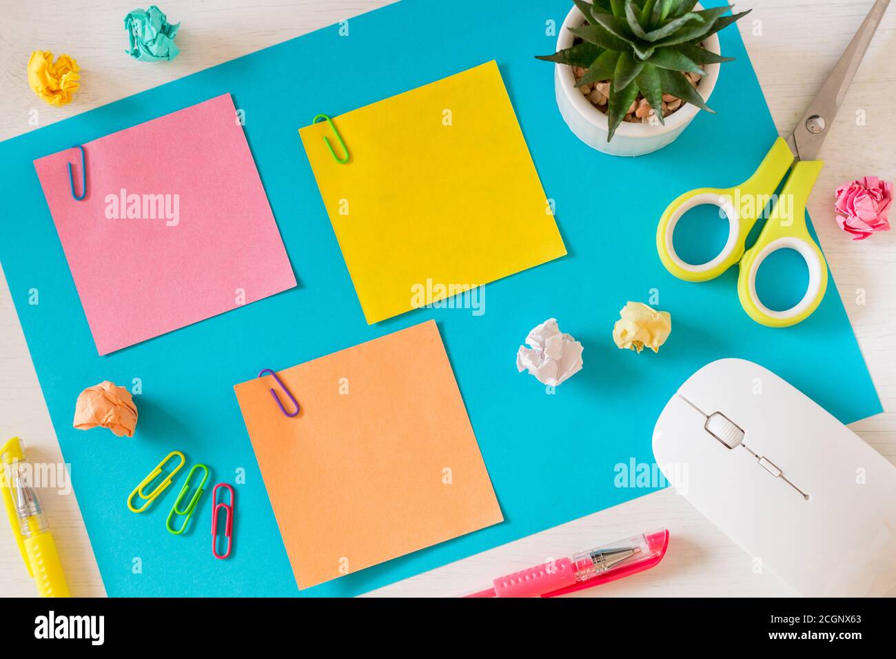 Eine große, blaue Karte auf dem Schreibtisch und drei kleine farbige Blätter mit Platz für Text. Büro- und Schulzubehör, Computermaus, Stifte, zerknittertes Papier Stockfoto