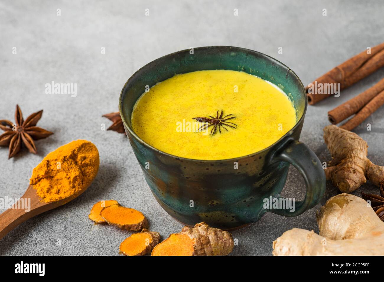 Traditionelles indisches Getränk Kurkuma Latte oder goldene Milch mit Zimt, Ingwer, Anis, Pfeffer auf betontem Hintergrund. Gesundes Herbst- oder Wintergetränk. cl Stockfoto