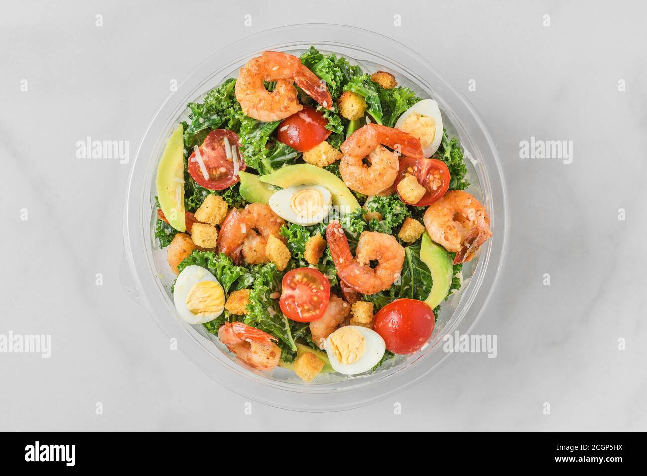 Plastikpaket mit gesunden Garnelen caesar Salat mit Avocado, Grünkohl, Tomaten und Eiern zum Mitnehmen. Draufsicht. mediterrane Ernährung Stockfoto