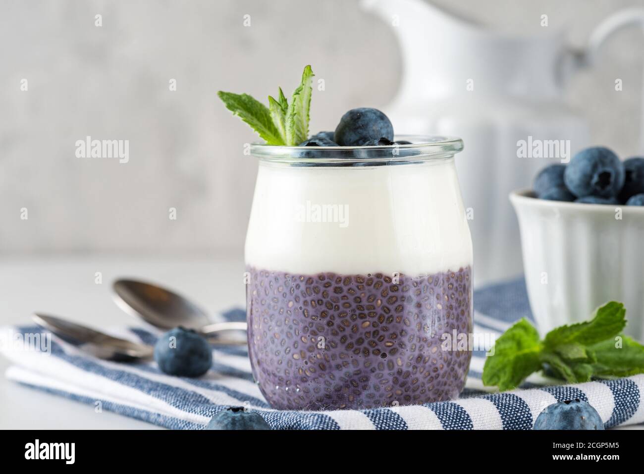 Heidelbeer-Joghurt-Parfait mit Chia-Pudding, Kokosjoghurt, frischen Beeren und Minze im Glas für gesundes Diätfrühstück auf Serviette über Marmortisch Stockfoto