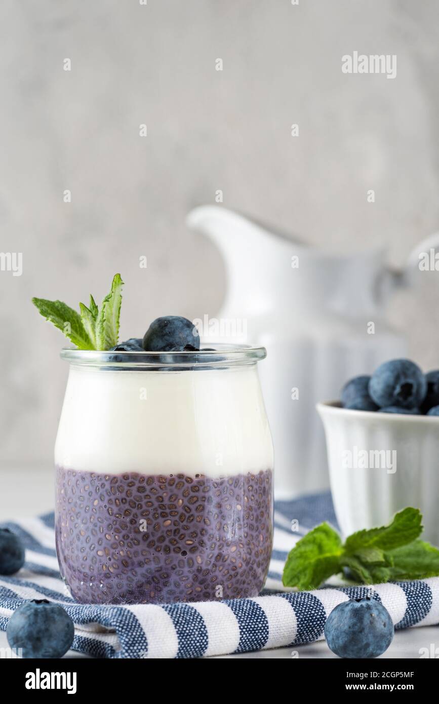 Gesundes veganes Frühstück aus Heidelbeer-Parfaits mit frischen Beeren, Kokosjoghurt, Chia Pudding und Minze in einem Glas über Serviette auf weißem Tisch. ve Stockfoto