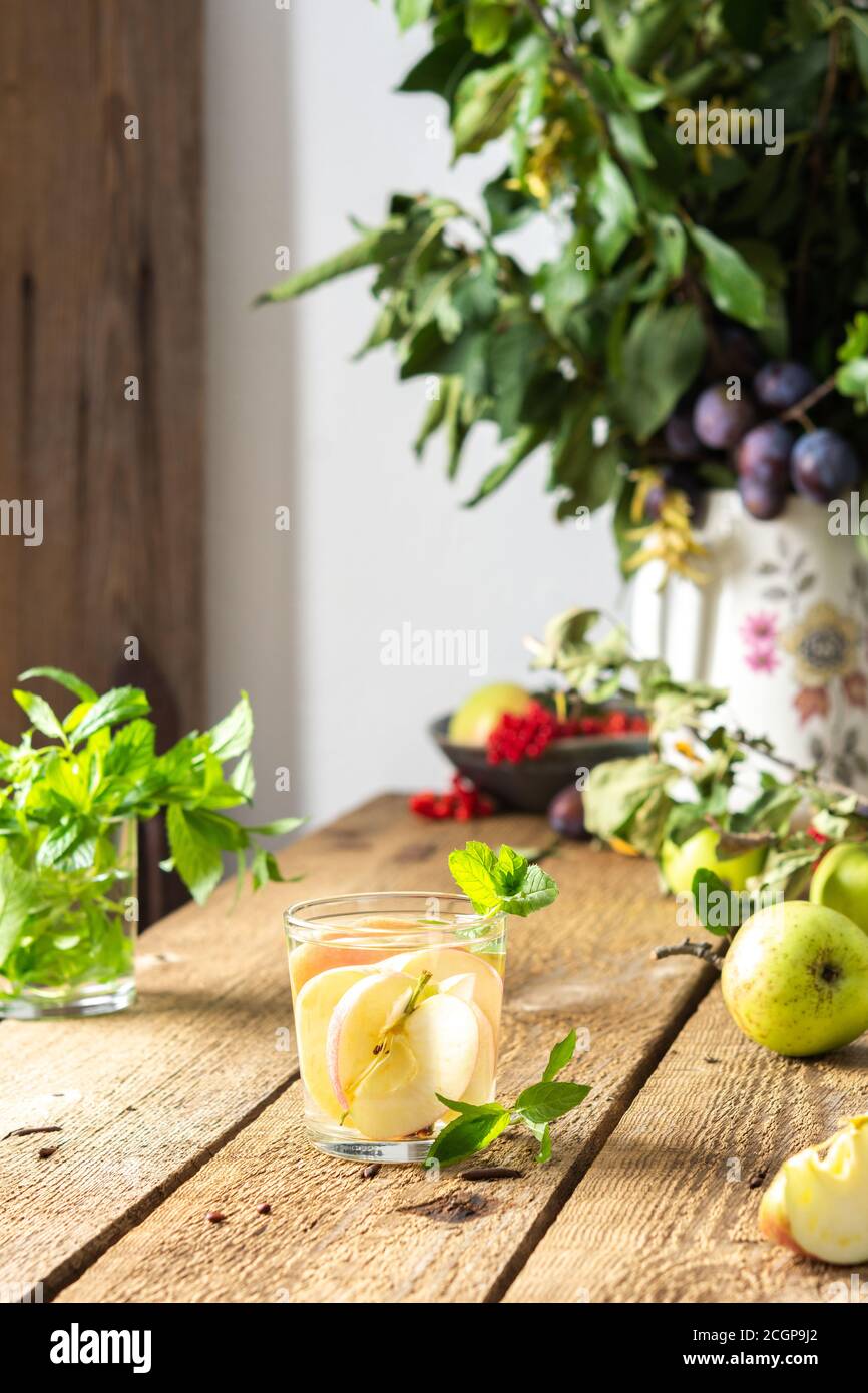 Herbst Apfelgetränk, Apfelscheiben mit Saft und Minze in einem Glas auf einem Holztisch, Blätter in einer Vase, Morgen im Dorf, rustikales Konzept Stockfoto