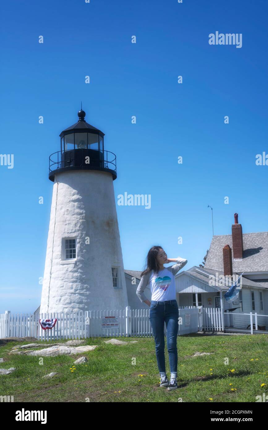 Eine chinesische Frau, die an einem sonnigen blauen Himmel in der Nähe des ikonischen pemaquid Point Leuchthauses in Bristol Maine steht, mit geschlossenen Augen, die ihr Haar fixieren. Stockfoto