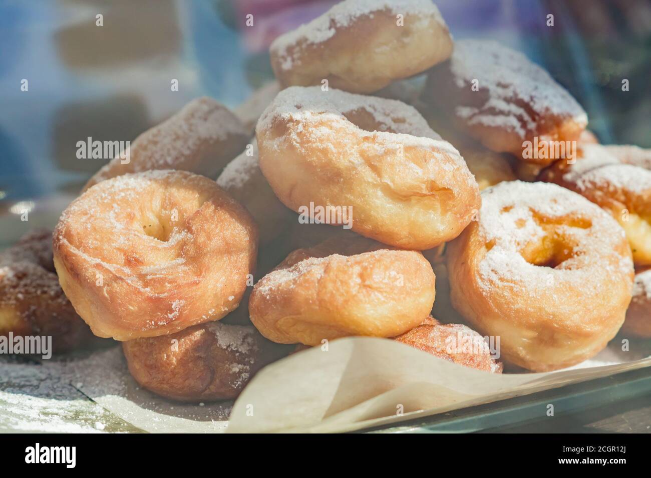 Die Pile der frischen frittierten Donuts, die mit dem Zuckerpulver auf dem Pergament bedeckt sind, die Süßigkeiten im Café-Schaufensterladen Stockfoto
