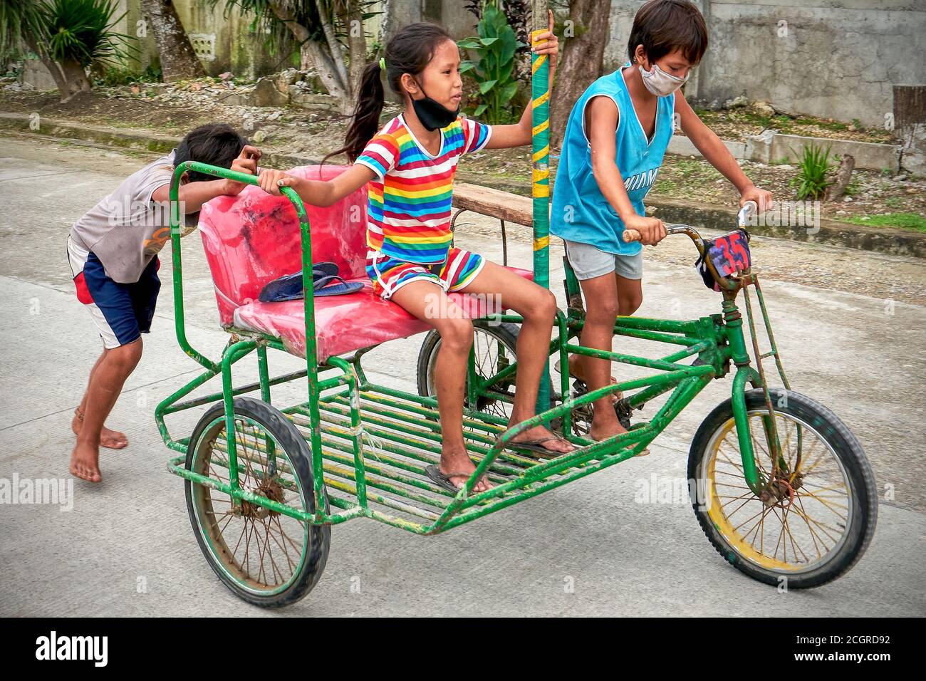 Drei barfuss kleine Kinder tragen Gesichtsmaske Reiten eine traditionelle bunte gemalt Pediküre auf einer Straße auf Boracay Insel, Philippinen, Asien Stockfoto