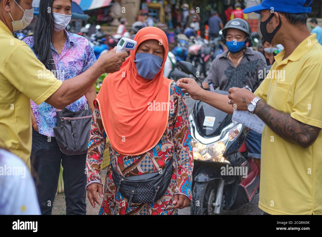 Beim Eintritt in einen Markt in Phuket Town, Thailand, lässt eine bunt gekleidete muslimische Frau ihre Temperatur überprüfen, um einen (Covid-19) Abfertigungsaufkleber zu erhalten Stockfoto