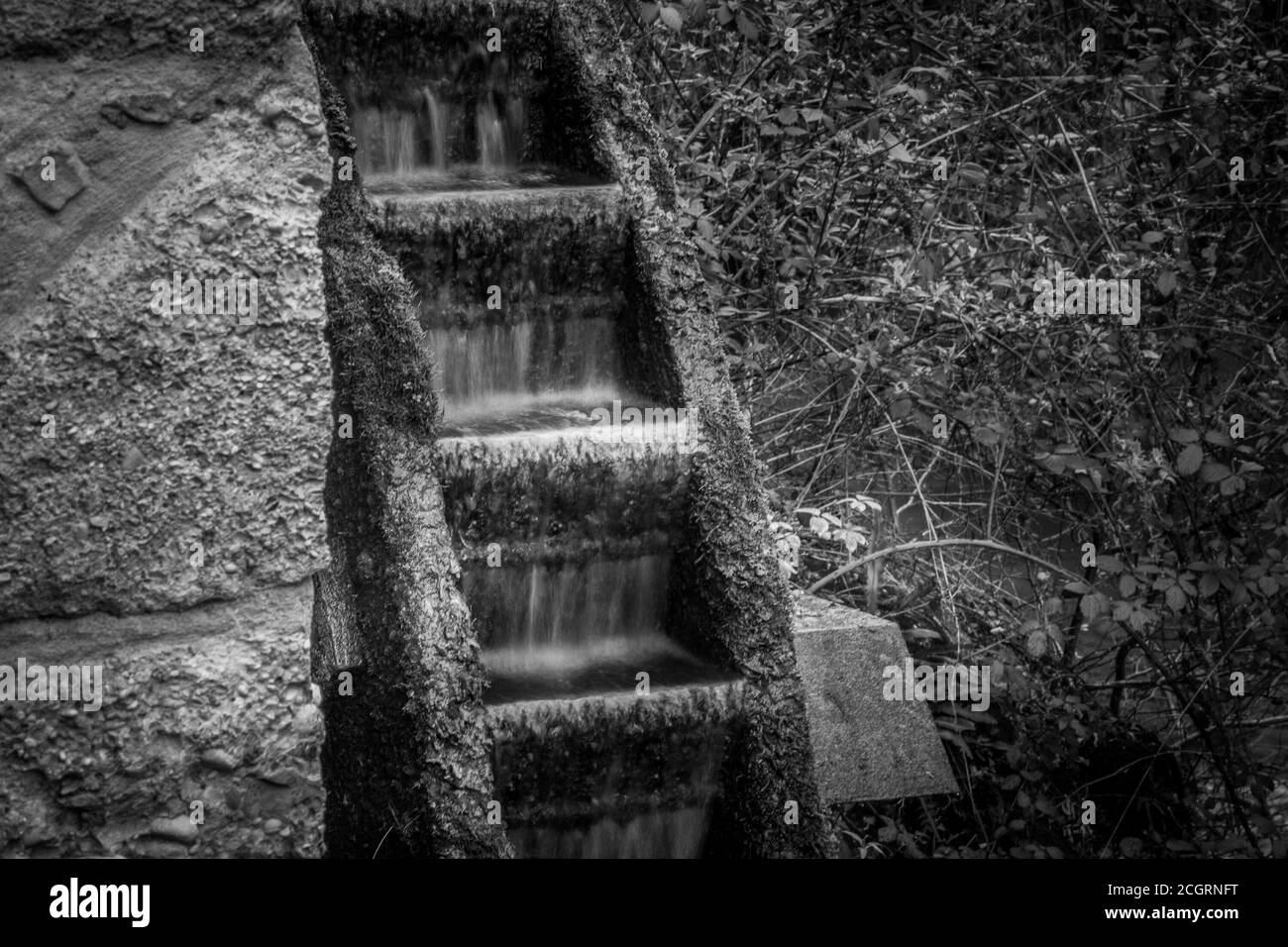 Schwarz-Weiß-Effekt des Wassers, das in ein fließt Uraltes Mühlrad Stockfoto