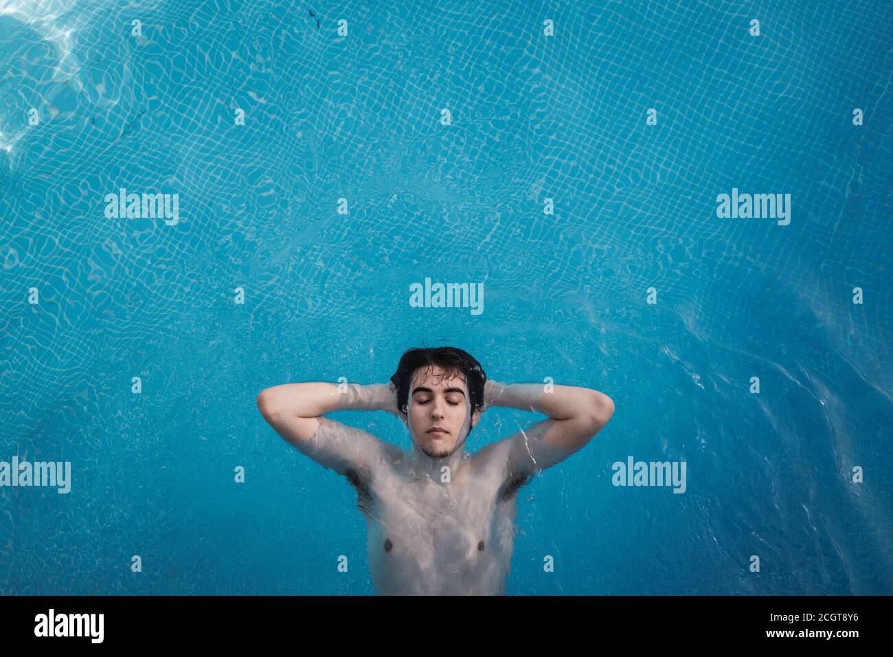 Draufsicht auf einen jungen Mann mit geschlossenen Augen, der in einem Schwimmbad mit den Händen im Hinterkopf schwimmt. Genießen Sie Urlaub beim Sonnenbaden Stockfoto