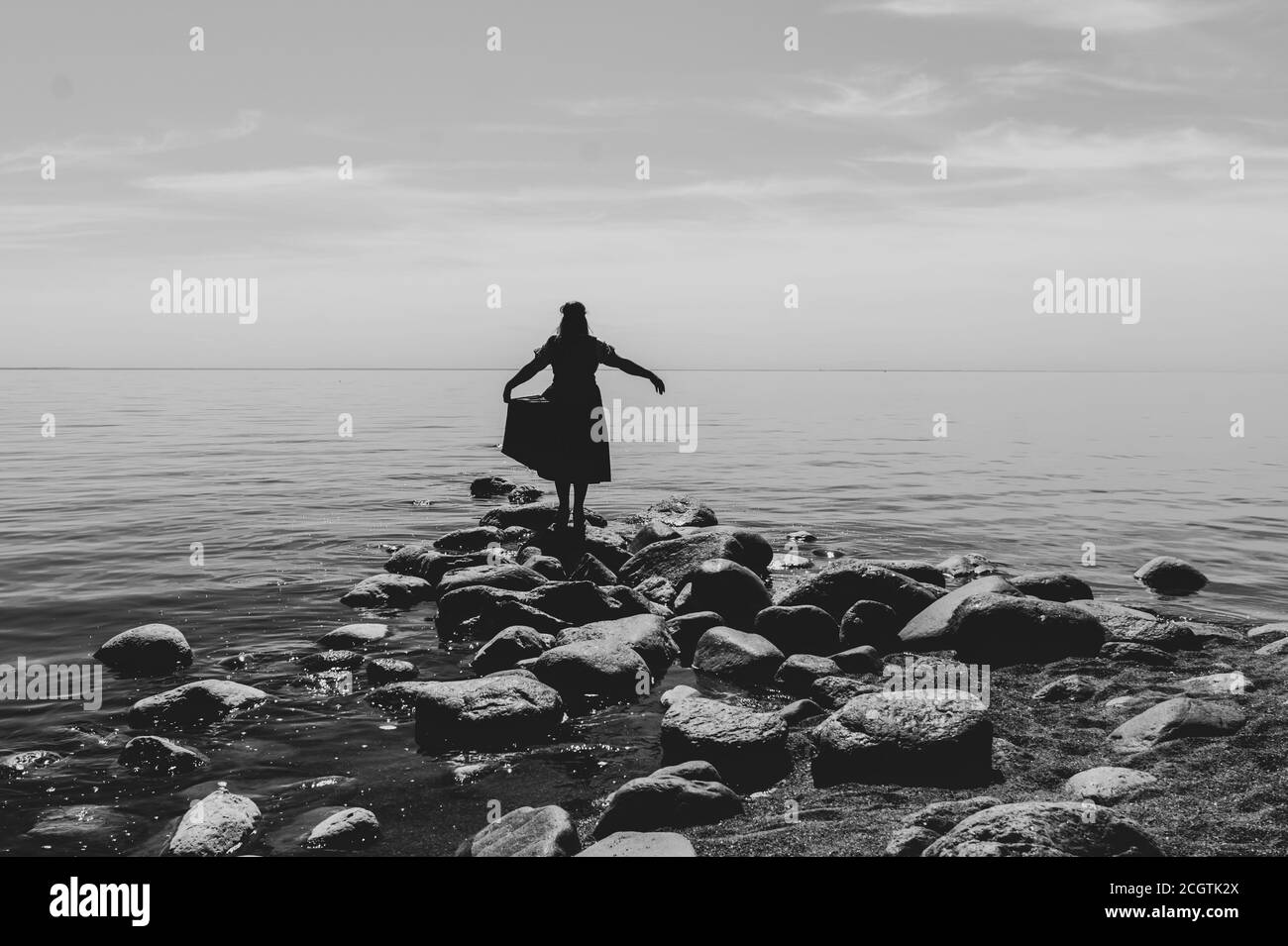 Silhouette einer Frau auf Steinen am Strand. Schöne Sommerlandschaft mit Horizont Linie. Schwarz und weiß Stockfoto