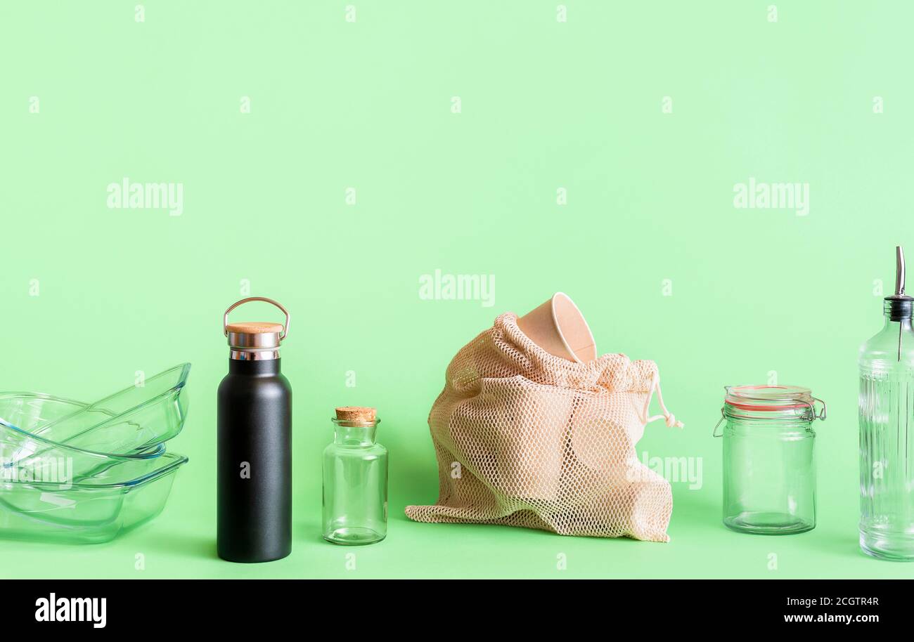 Nachhaltiges Lifestyle-Konzept mit Glasobjekten, Thermoskannen und biologisch abbaubaren Kaffeetassen, isoliert auf grünem Hintergrund. Haushaltsprodukte ohne Plastik Stockfoto