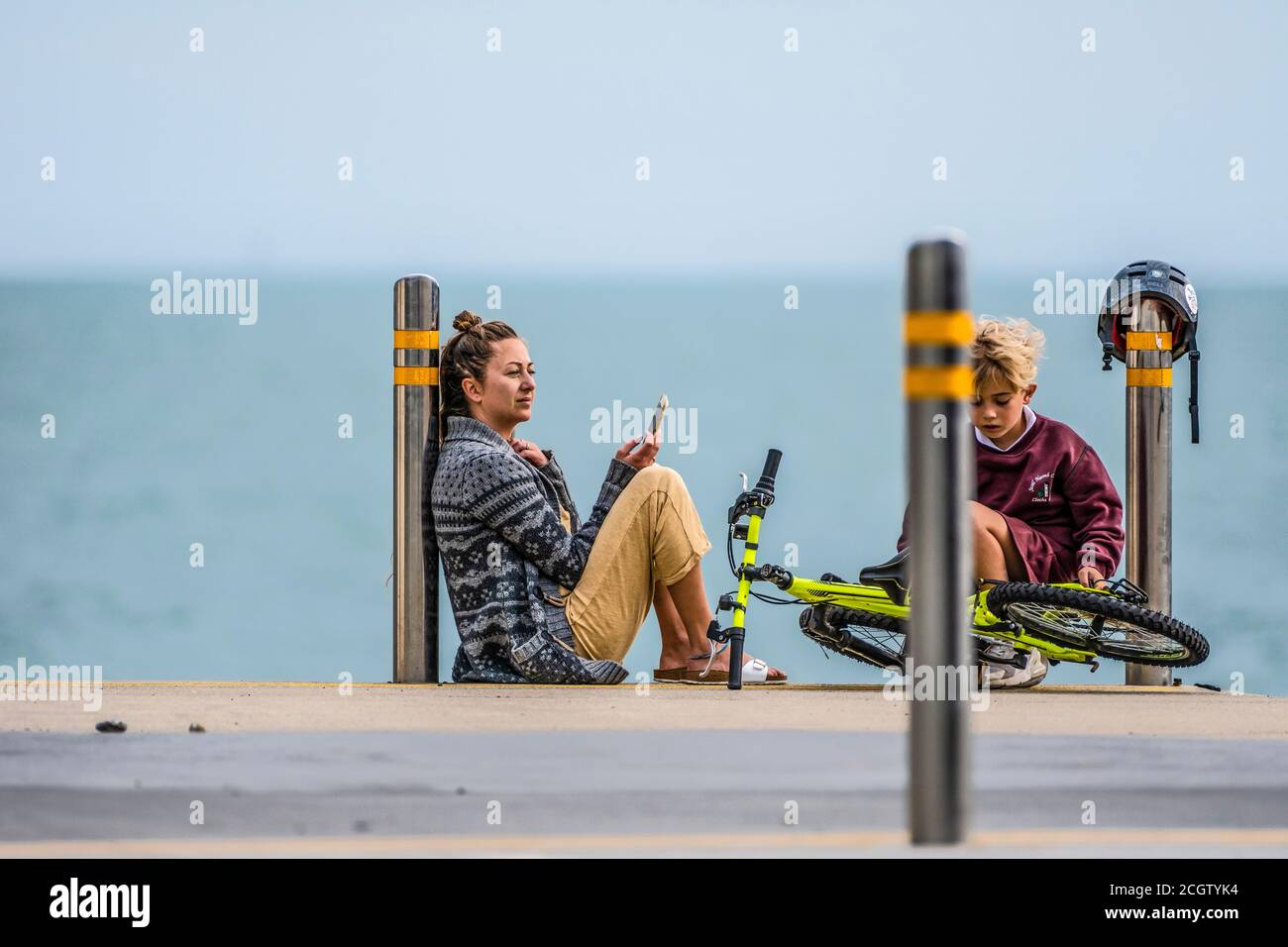 Moment des Restes. Mutter mit Handy am Meeresufer sitzend, spricht mit ihrem Sohn. Stockfoto