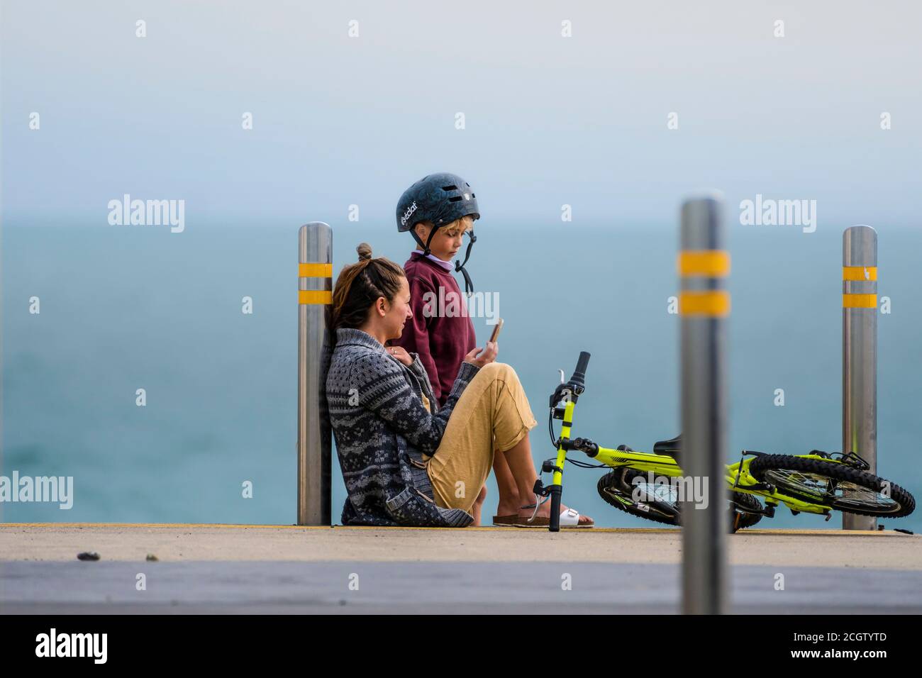 Moment des Restes. Mutter mit Handy am Meeresufer sitzend, spricht mit ihrem Sohn. Stockfoto