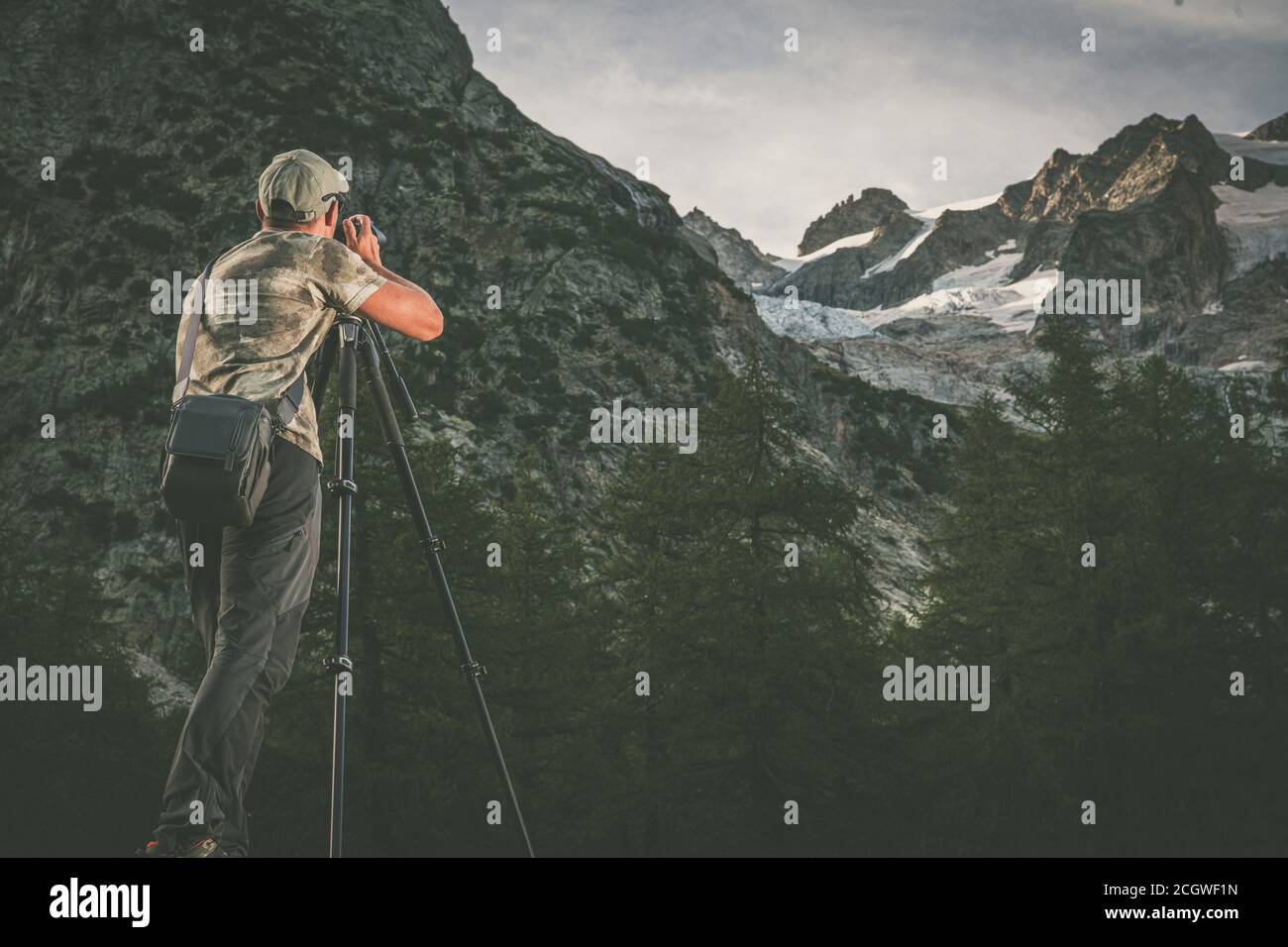 Kaukasischer Naturfotograf in den 40er Jahren mit alpinen Landschaftsbildern Verwenden einer professionellen Digitalkamera, die im Sommer auf einem Stativ installiert ist Abend Stockfoto