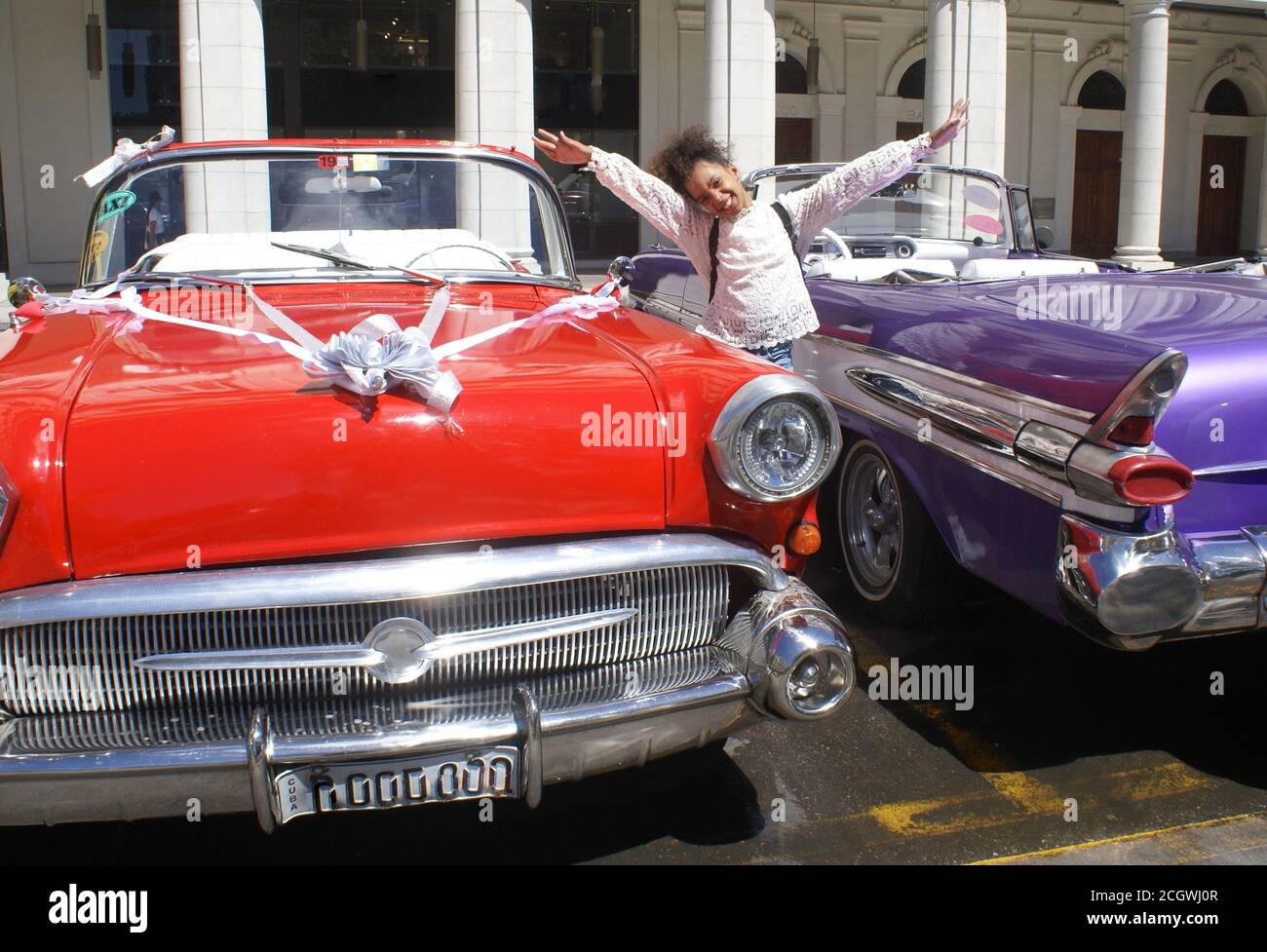 Kuba, La Havana-29/03/2019. Kleines Mädchen kreolisch lächelnd glücklich zwischen zwei clasic Auto in der Stadt Straße .to redaktionelle Verwendung. Keine Modellfreigabe Stockfoto