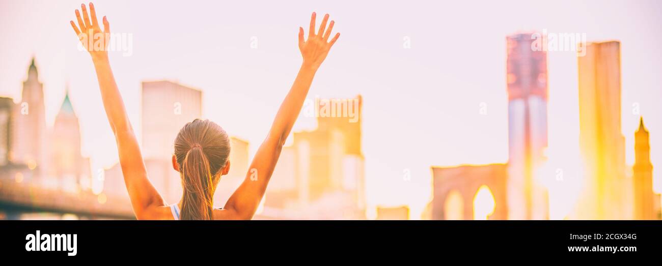 Glücklicher Erfolg Gewinnerin Frau mit aufgeweckten Armen in Freude am Sonnenuntergang der Skyline von New York City. Banner Panorama der Innenstadt Gebäude Stadtbild, Person aus Stockfoto