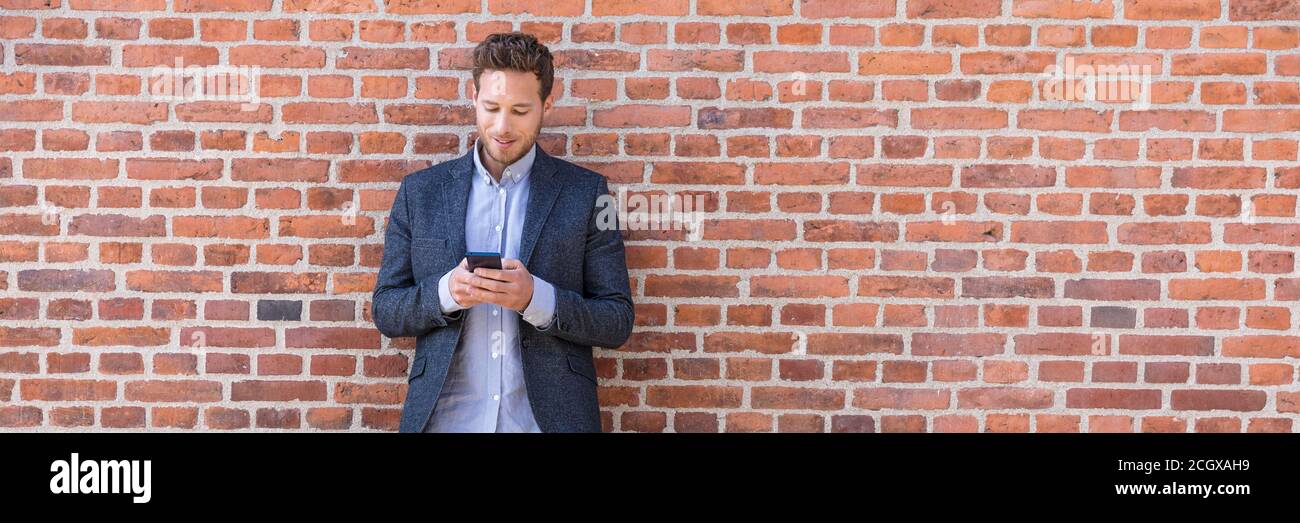 Geschäftsmann sms SMS-SMS-Handy-App in der Stadt Straße auf Backsteinmauer Hintergrund. Business-Mann hält Smartphone in Smart Casual Wear stehen. Urban Young Stockfoto