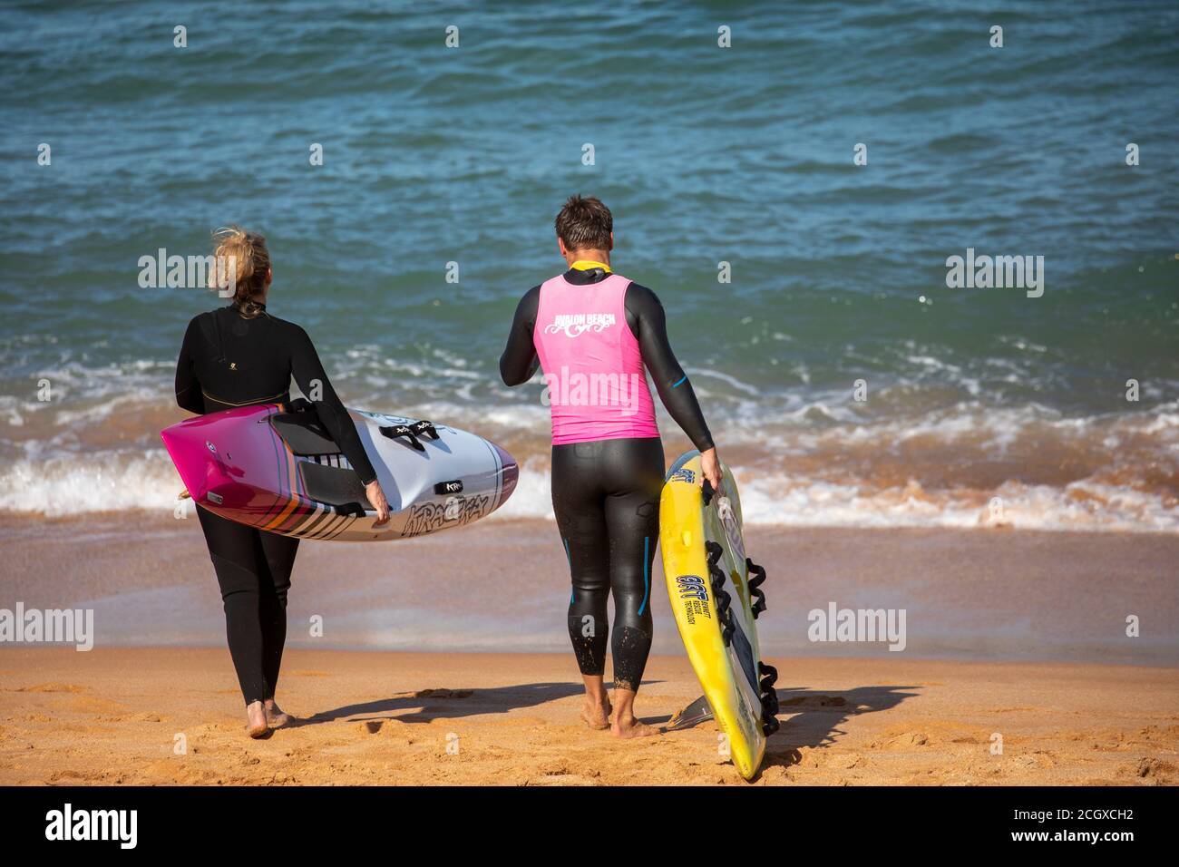 Mann und Frau tragen Neoprenanzüge am Strand mit ihren Surfbrettern, Sydney, Australien Stockfoto